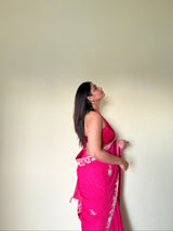 Woman wearing a pink saree with a white border against a plain background