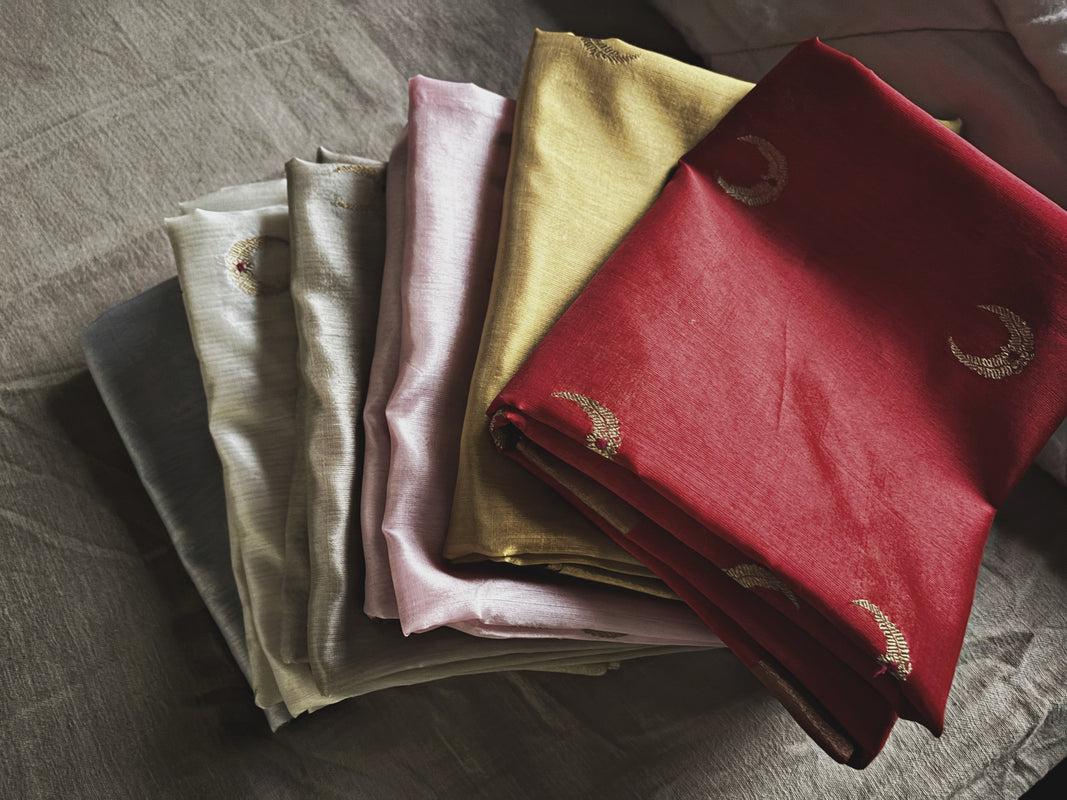 Stack of folded dupattas in various colors on a textured surface